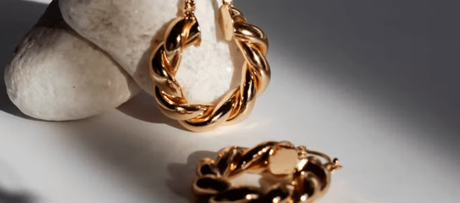 Chunky gold twisted bracelet beside a pale stone